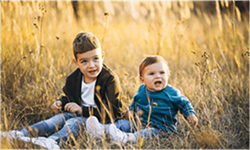 Two young children sitting in a grassy field during golden hour.