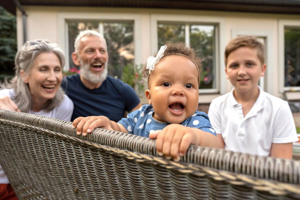 A joyful multigenerational family with a baby, a boy, and two older adults smiling outdoors.