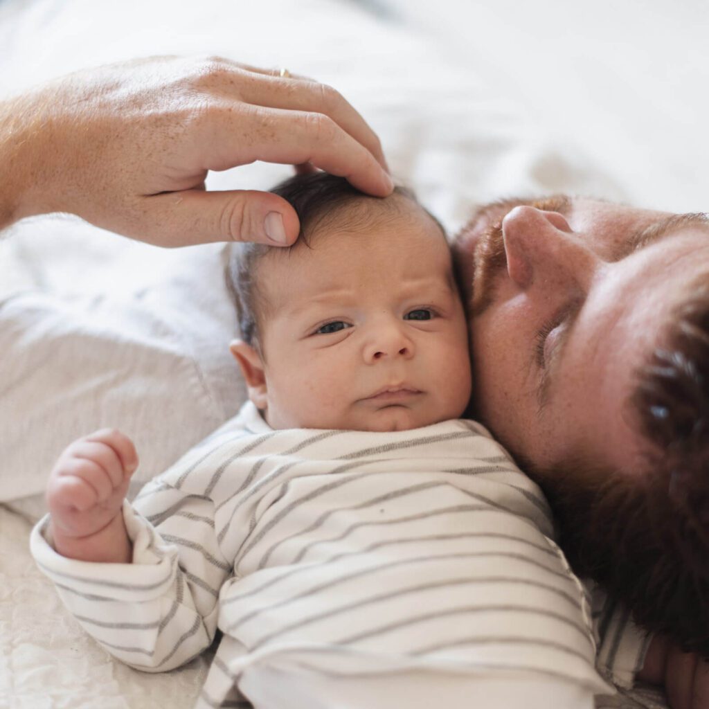 Father gently touching baby's head while lying close together.