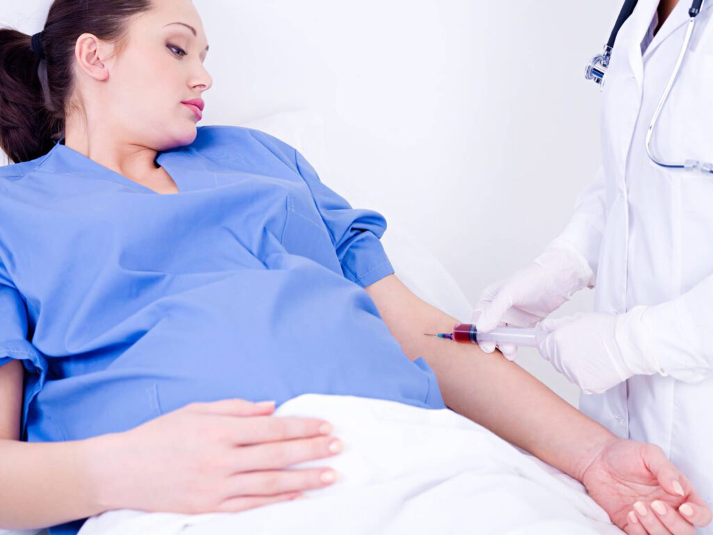 A healthcare professional draws blood from a patient lying in a hospital bed.