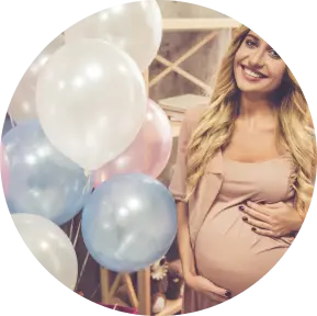 A smiling pregnant woman holding her belly, surrounded by pastel balloons.