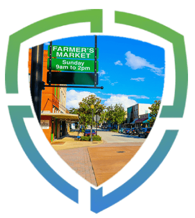 Shield-shaped sign indicating "farmer's market sunday 9am to 2pm" with a background of a sunny street scene.